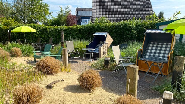 A garden area with outdoor seating, including chairs and a table, surrounded by sand and plants. - Vacation apartment Robbe in house Alina (Büsum)