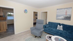 A living room with a blue sofa, a grey armchair, a small table, and a painting of a lighthouse. - Vacation apartment Robbe in house Alina (Büsum)
