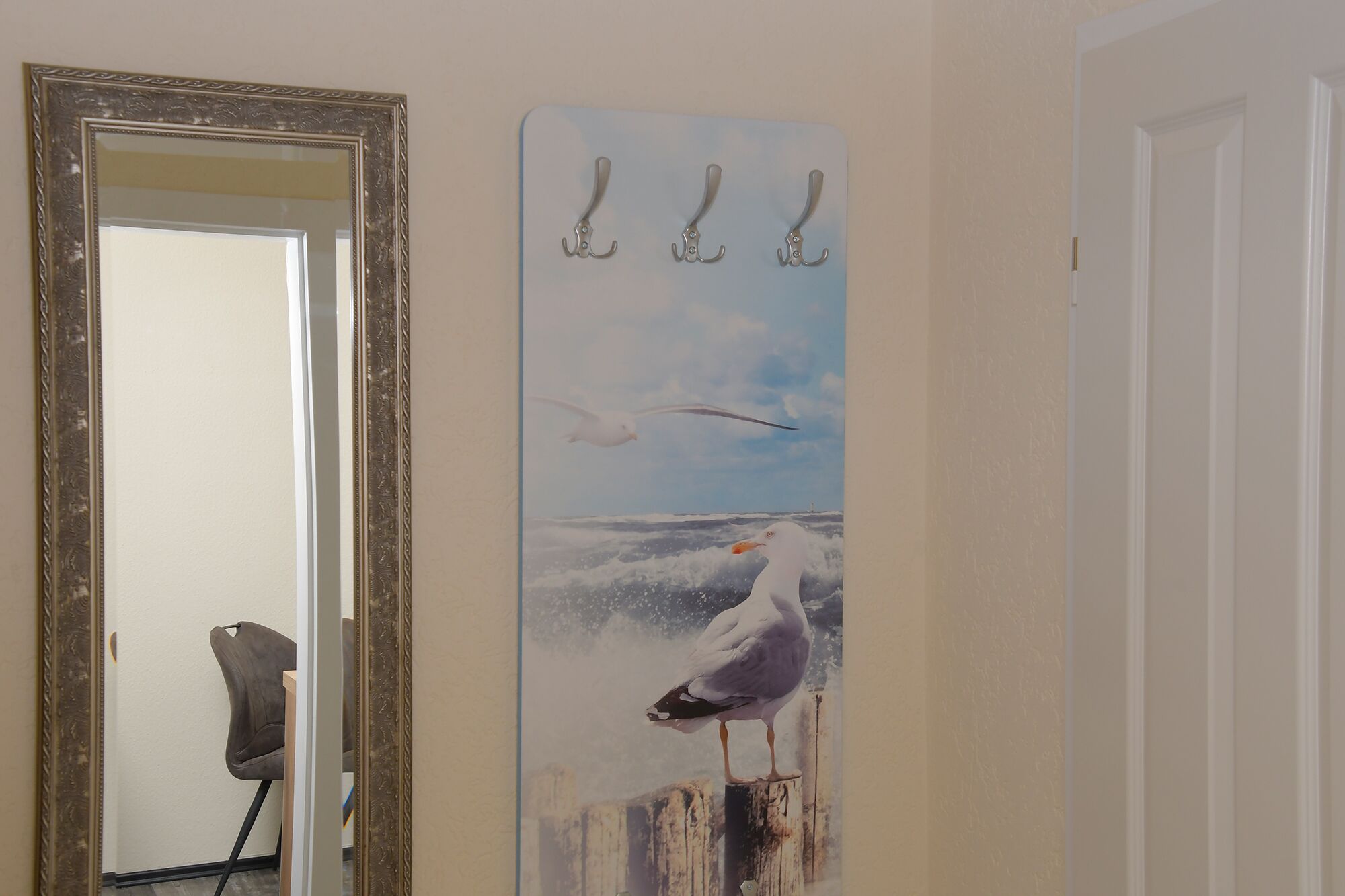 Een gang met een spiegel, een schilderij van meeuwen en een kapstok.