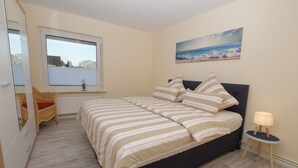 A bedroom with a bed, a window, a painting, and a bedside table with a lamp. - Vacation apartment Robbe in house Alina (Büsum)