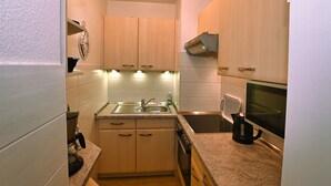 Una cocina compacta con armarios de madera clara, un lavamanos de acero inoxidable, una cafetera y un microondas.