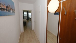 A hallway with a wooden door, a mirror, and a painting of a harbor scene. - Herzlich Willkommen in der der Ferienwohnung "meerblick 9"! (Büsum)
