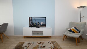 A living room with a flat-screen TV on a white TV stand, a grey armchair with a colorful pillow, and a patterned rug on the floor. - Herzlich Willkommen in der der Ferienwohnung "meerblick 9"! (Büsum)
