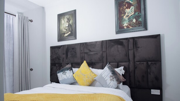 A bedroom with a large bed, a headboard, and two framed pictures on the wall. - Luxury 2 Bed Self Catering Apartment in Masvingo (Masvingo)