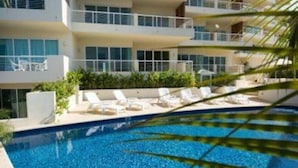 A multi-story hotel with a swimming pool surrounded by palm trees.