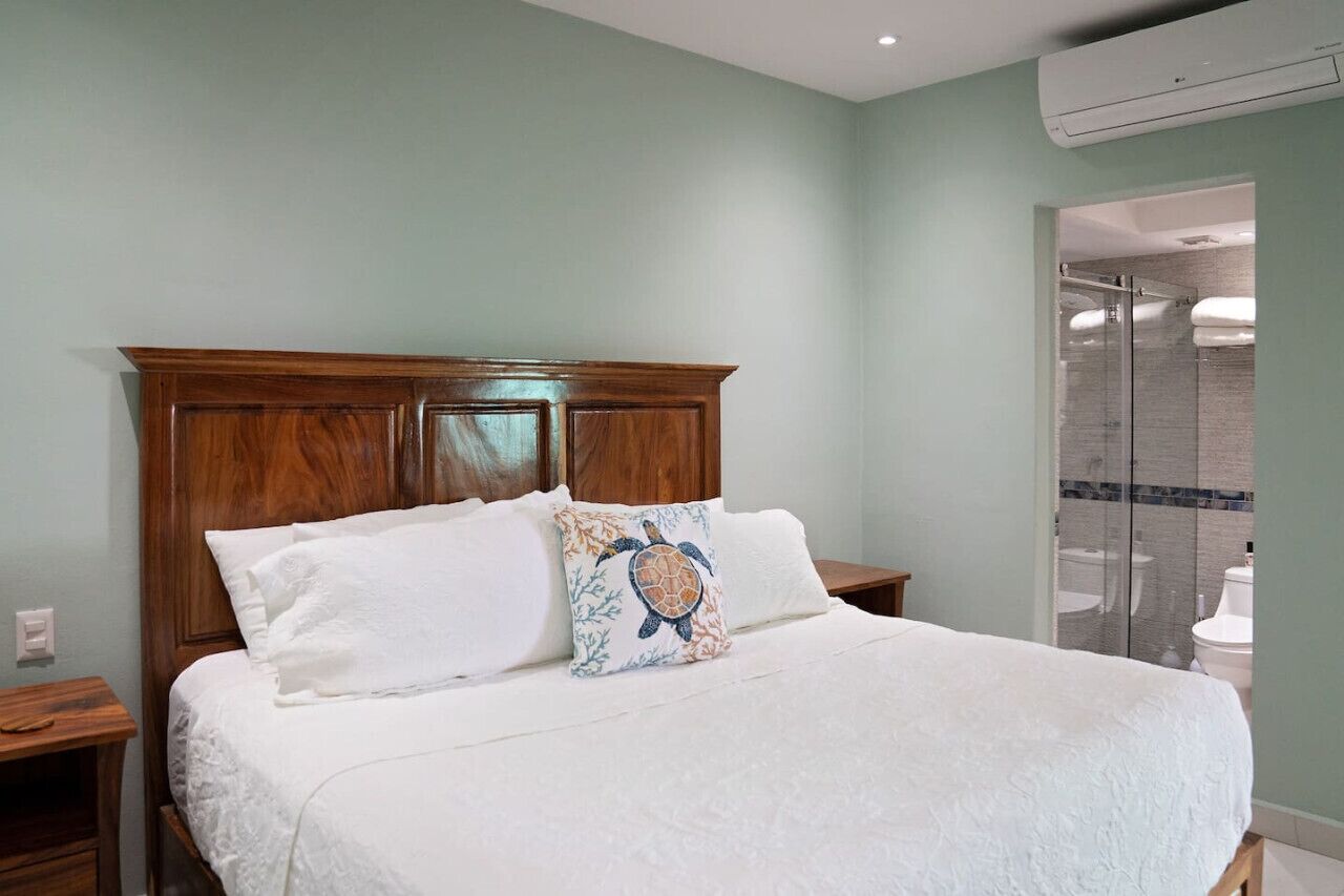 A bedroom with a wooden headboard, a bed with white linens, and a bathroom with a glass shower enclosure.