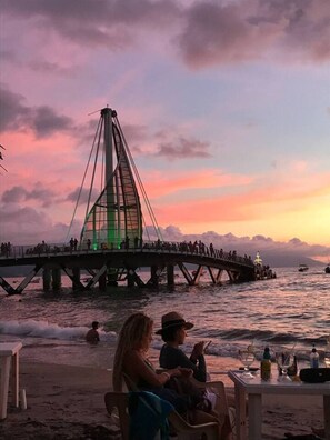 A coastal scene with a bridge, beach, and people.