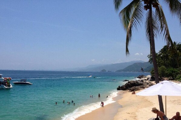A beach with clear water, boats, and people swimming.