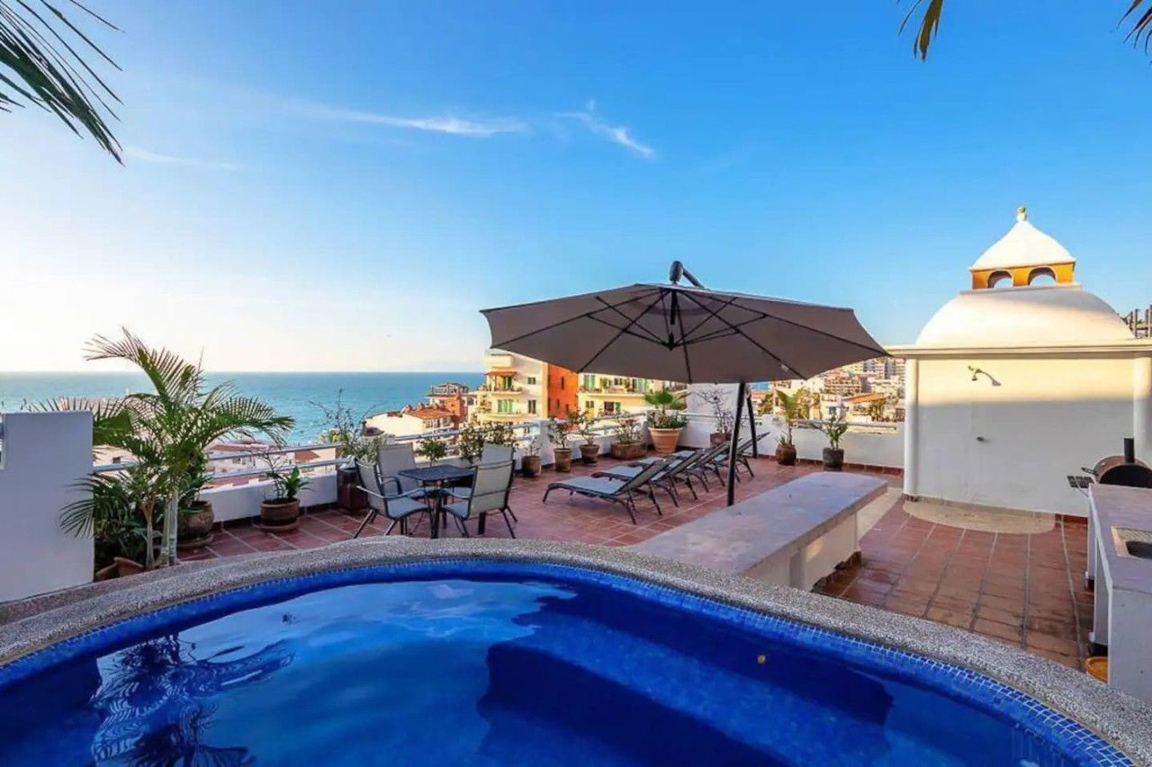 Un espace piscine aménagé sur le toit, offrant une vue sur la mer, avec des chaises longues et des parasols.