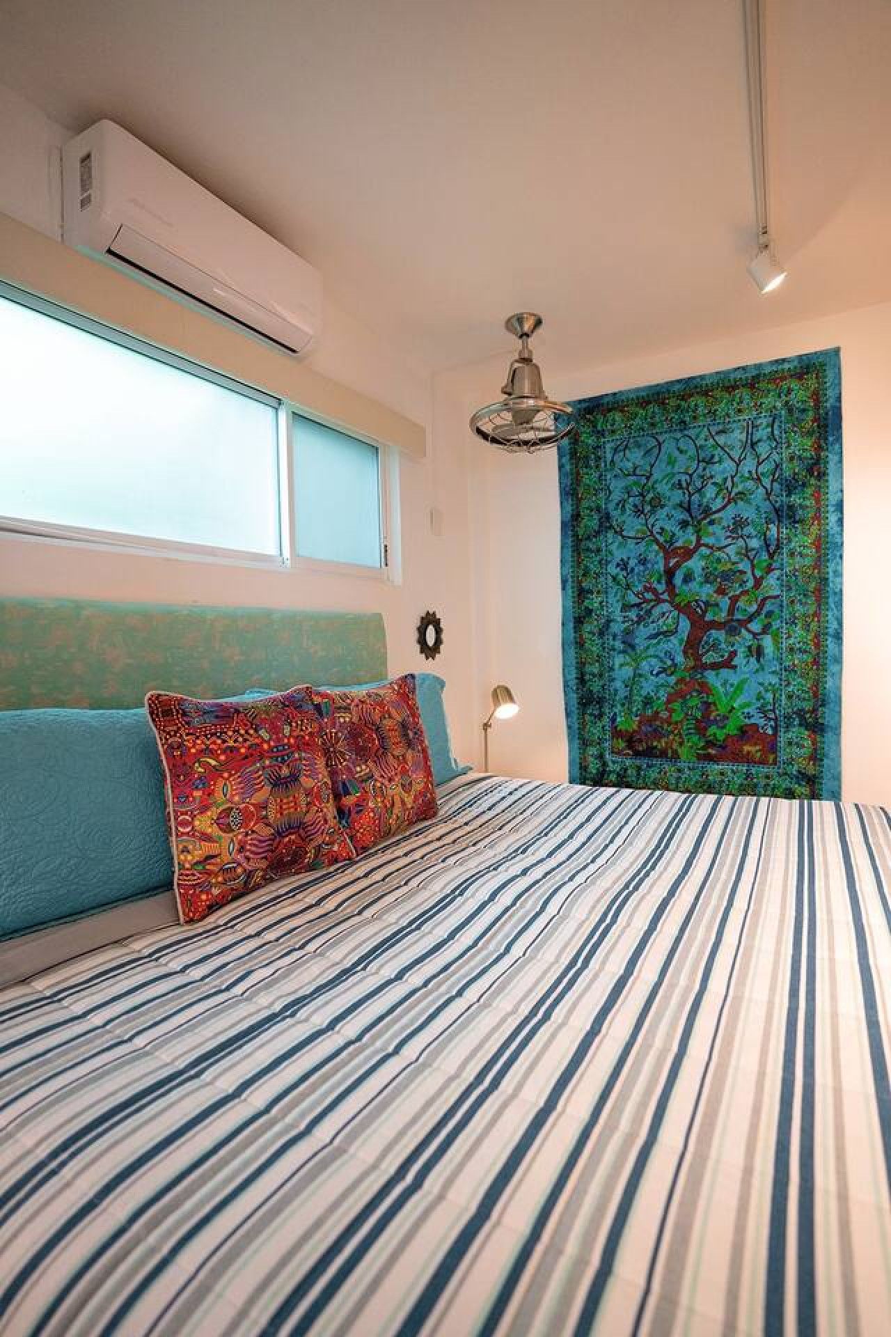 Ein Schlafzimmer mit Bett, Fenster, Klimaanlage, Deckenventilator und Wandteppich.