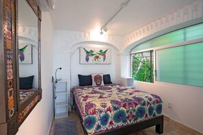 A bedroom with a bed, a dresser, a mirror, and a window with a view of greenery.