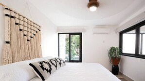 A bedroom with a bed, a macrame wall hanging, a potted plant, and a window with a view of greenery. - Beautiful Vallarta View Condo*********** (Puerto Vallarta)
