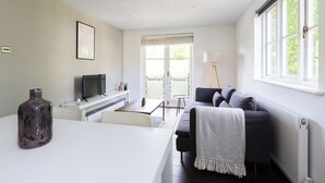 A modern living room with a sofa, a coffee table, a TV, and a large window with blinds. - The Imperial Wharf Collection (London)