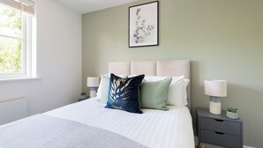 A neatly made bed with a patterned bedspread, two bedside lamps, and a small potted plant on a bedside table. - The Imperial Wharf Collection (London)
