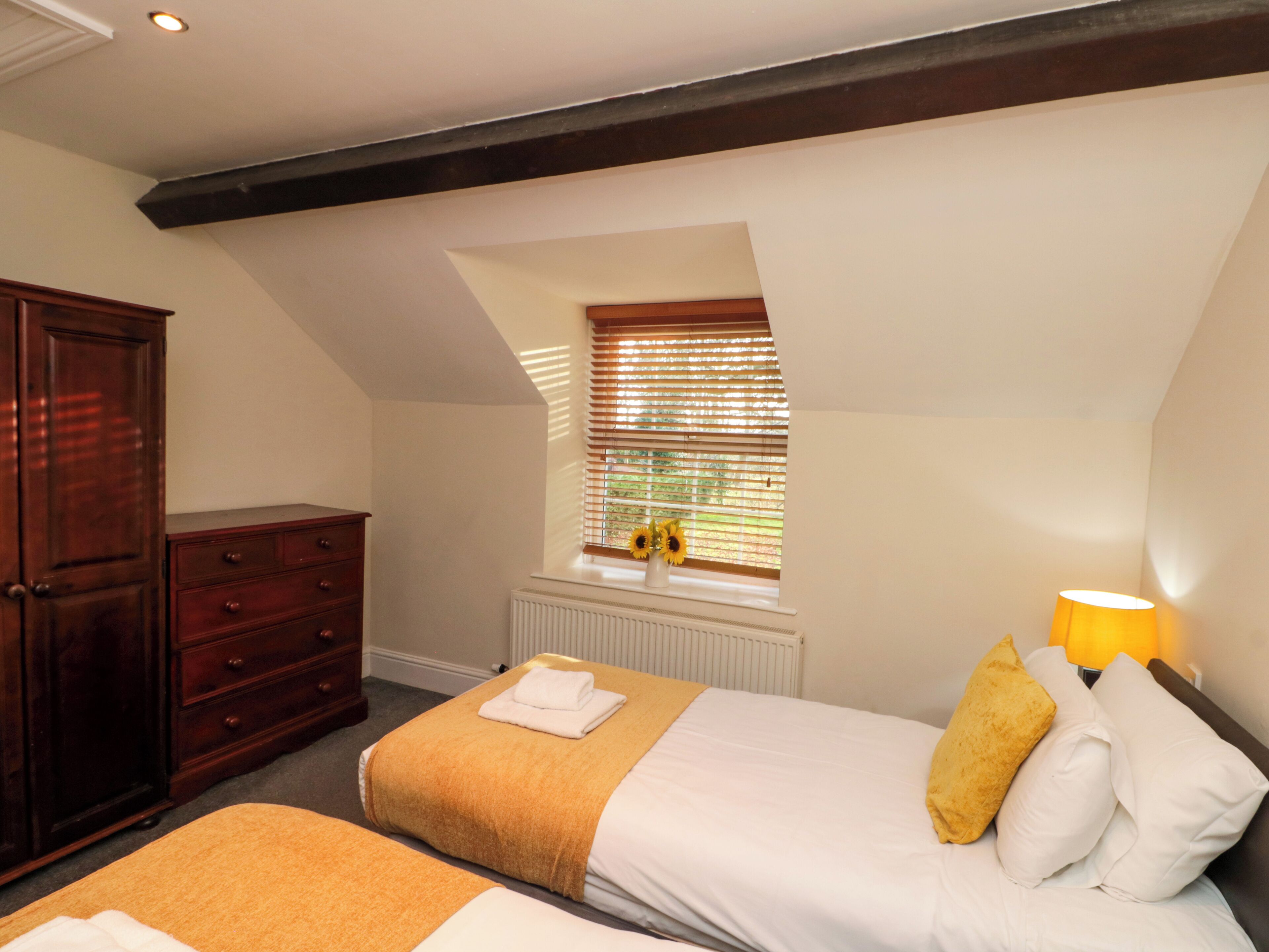 A bedroom with two beds, a dresser, a window with blinds, and a radiator.