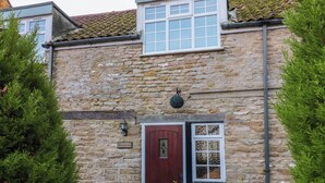 A stone building with a red door, a window with white framing, and a sign that reads "The Coachhouse". - The Coach House (Scarborough)