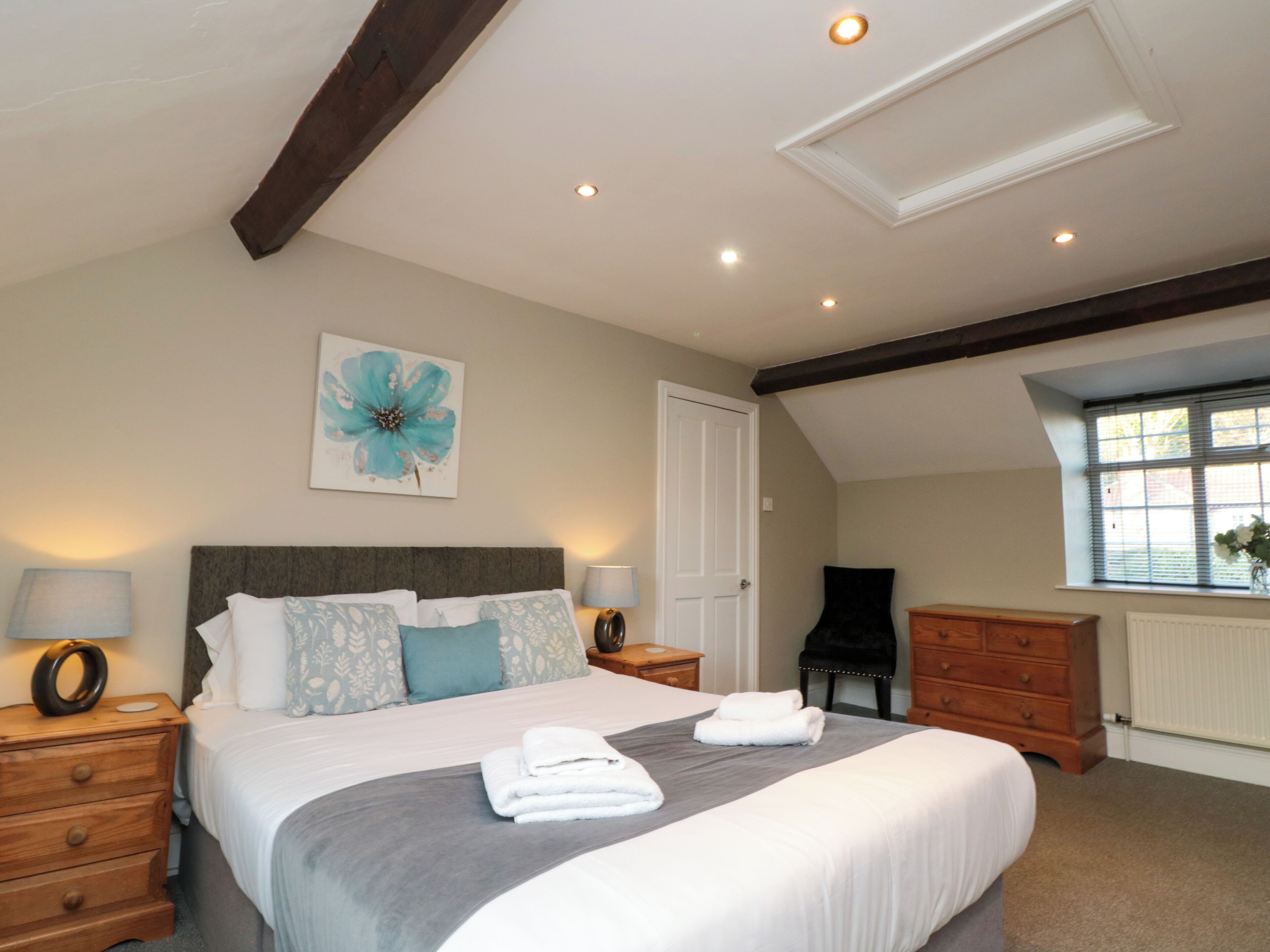 A bedroom with a large bed, bedside tables, a chair, a dresser, and a window with blinds.