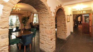 A stone archway leading to a dining area with a table and chairs, a Christmas tree, and a bar sign. - The Coach House (Scarborough)
