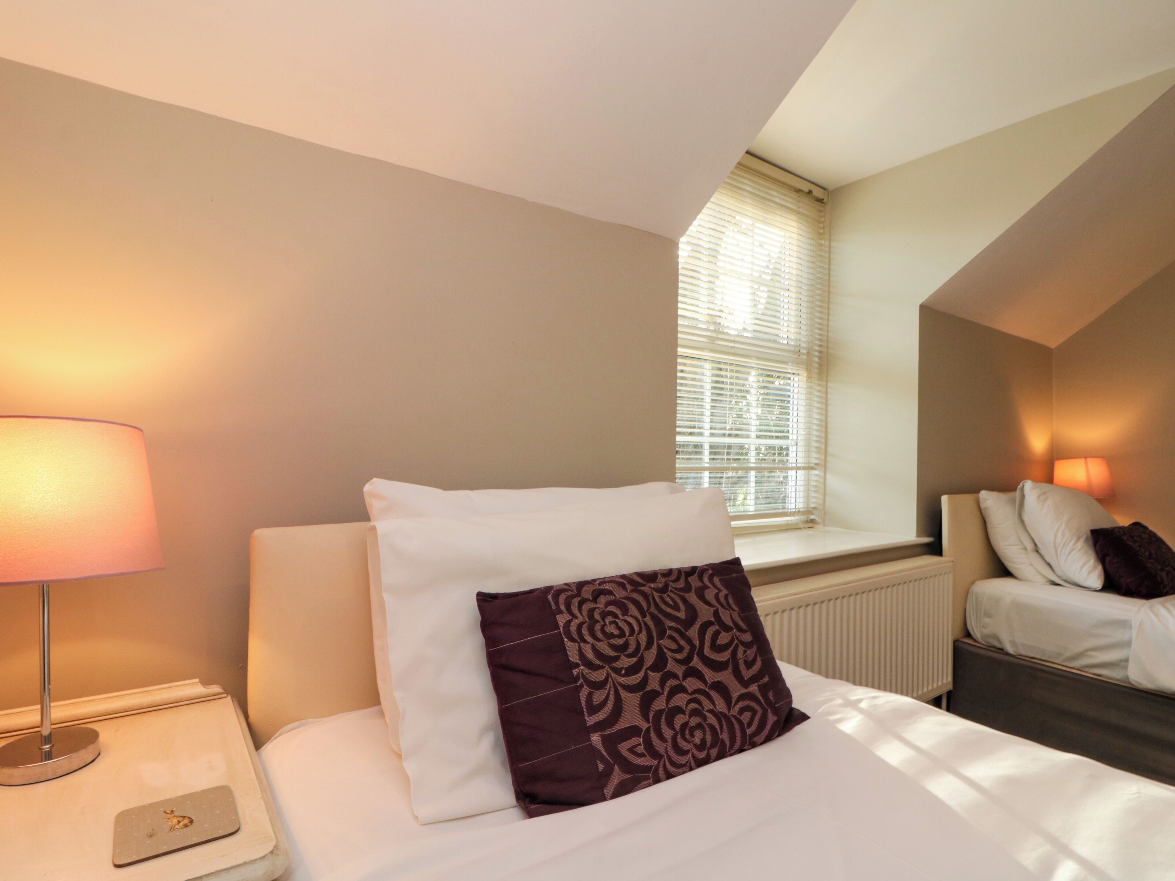 Een hotelkamer met een bed, een bedlamp, een raam met jaloezieën en een radiator.