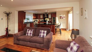 A modern living room with a brown sofa set, a dining area, and a kitchen in the background. - The Coach House (Scarborough)