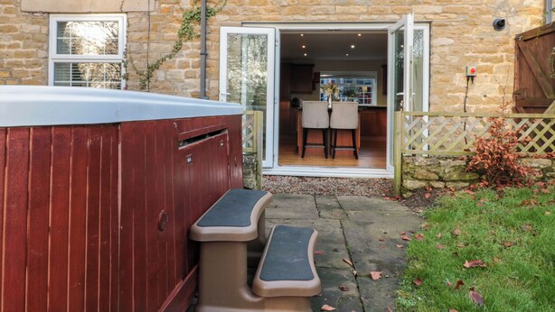A stone house with a hot tub, outdoor seating, and a view into the kitchen. - The Coach House (Scarborough)