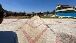 A paved walkway leading to a building with a red roof, surrounded by greenery and a clear sky. - Rangi Taranga (Chikkamagaluru)