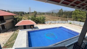 A swimming pool with a blue interior, surrounded by a covered patio area. - Rangi Taranga (Chikkamagaluru)