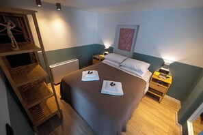 Un dormitorio con cama, mesitas de noche, una mesita auxiliar, un estante con un maniquí y una obra de arte en la pared.