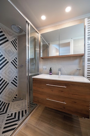 A bathroom with a shower, a vanity with a mirror, and a patterned floor. - Villa Vesta Retiré - Kalamata Mediterranean Suites & Villas (Kalamata)