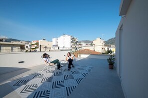 A rooftop terrace with a geometric patterned floor, two people seated on chairs, and potted plants. - Villa Vesta Retiré - Kalamata Mediterranean Suites & Villas (Kalamata)