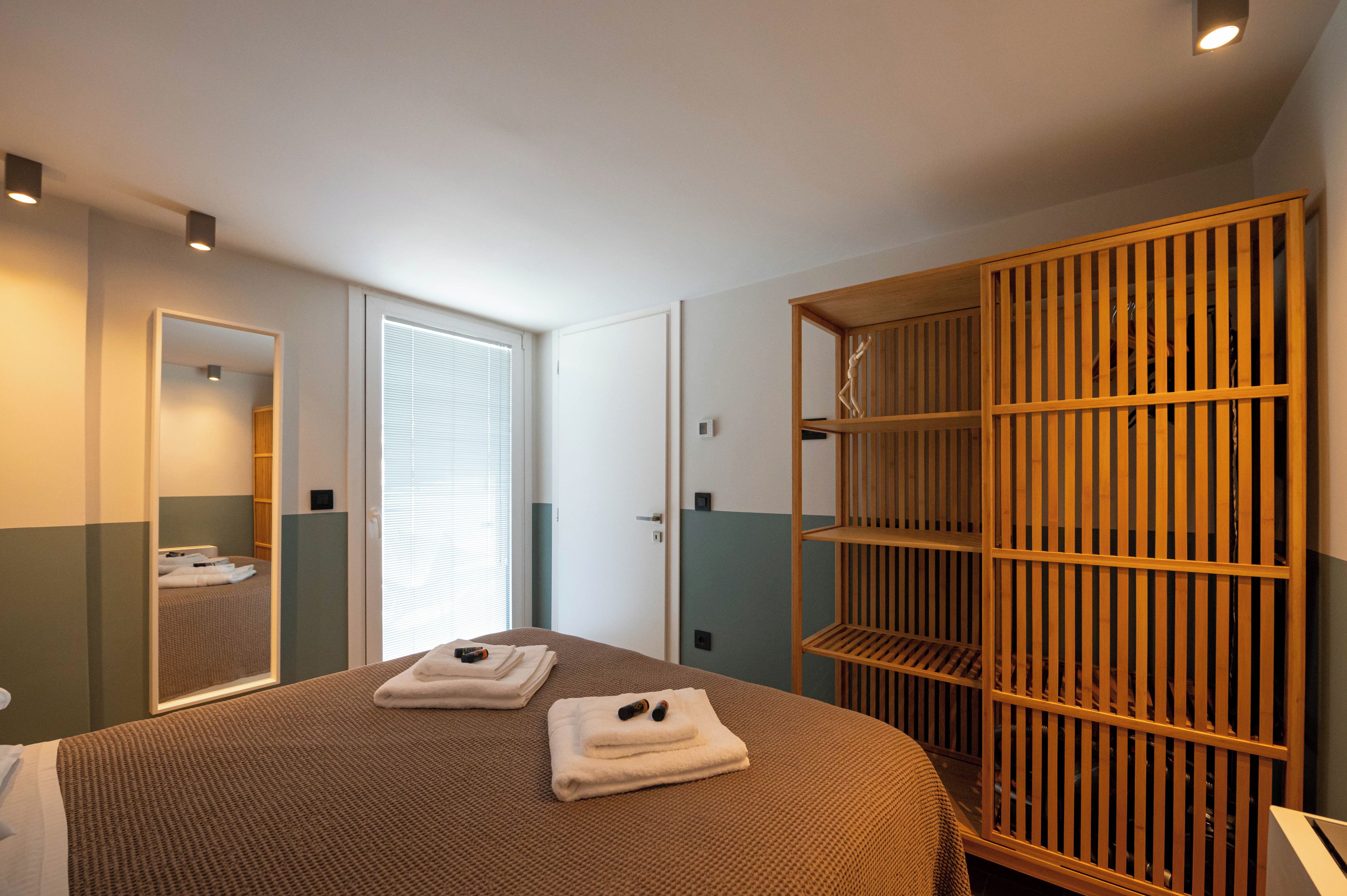 Ein Hotelzimmer mit Bett, Schrank, Spiegel und einer Tür zu einem anderen Raum.