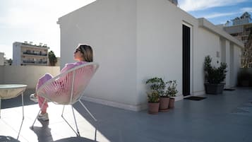 A person sitting on a chair on a rooftop terrace with potted plants and a table.