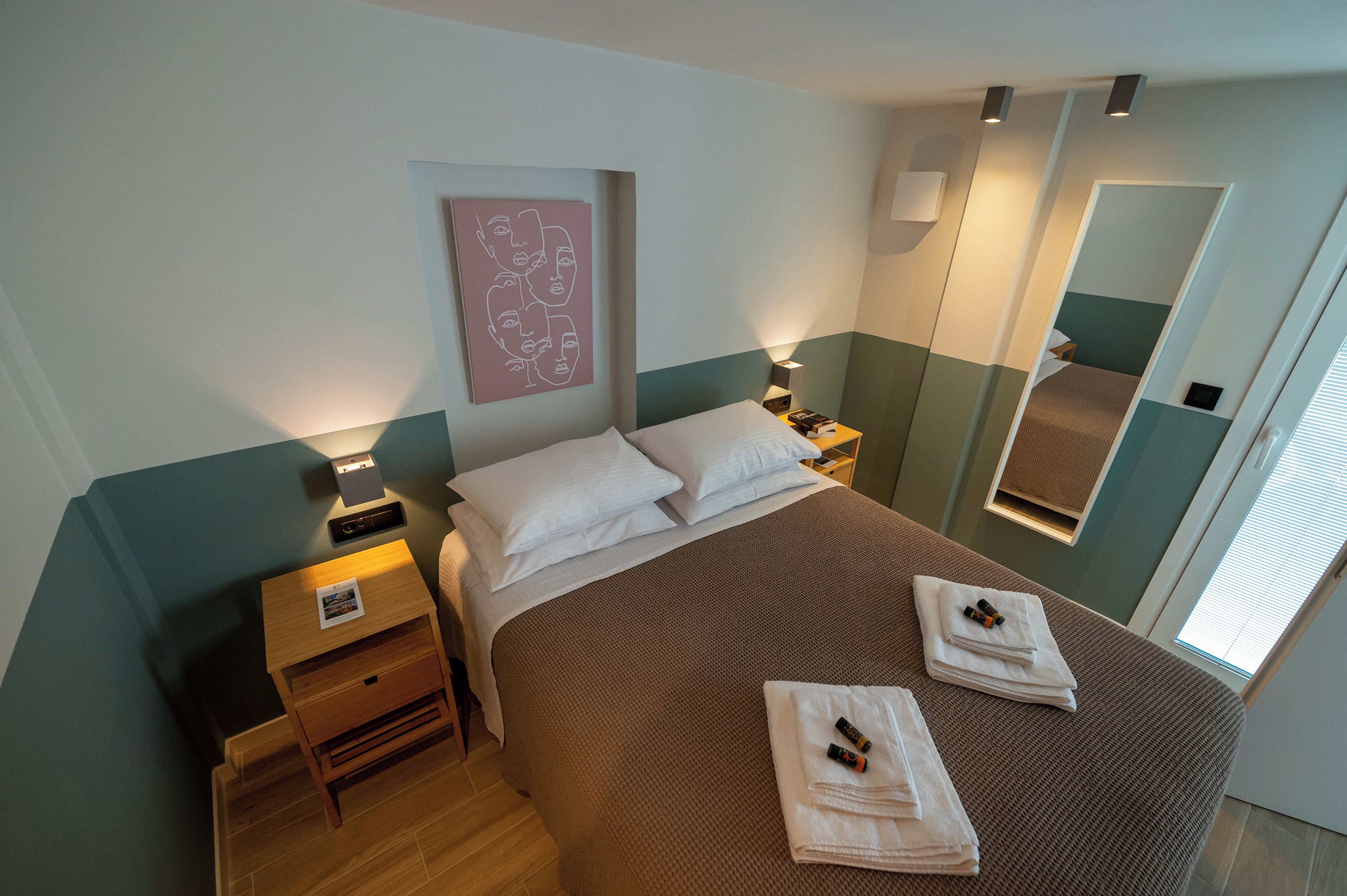 A hotel room with a bed, bedside tables, a mirror, and a wall art piece.
