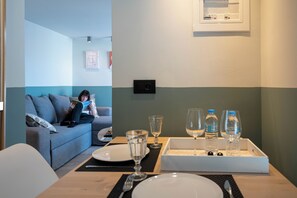 Una habitación con una mesa de comedor preparada para dos personas, un sofá y una lámpara fijada a la pared.