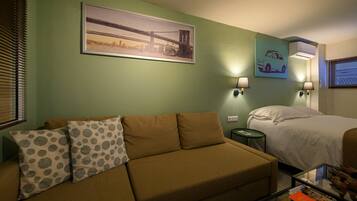 A room with a sofa, a bed, a framed picture of a bridge, and two wall-mounted lamps.