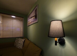 A room with a couch, a wall-mounted lamp, and a window with blinds. - Pols Studio - Project Kalamata Mediterranean Suites (Kalamata)