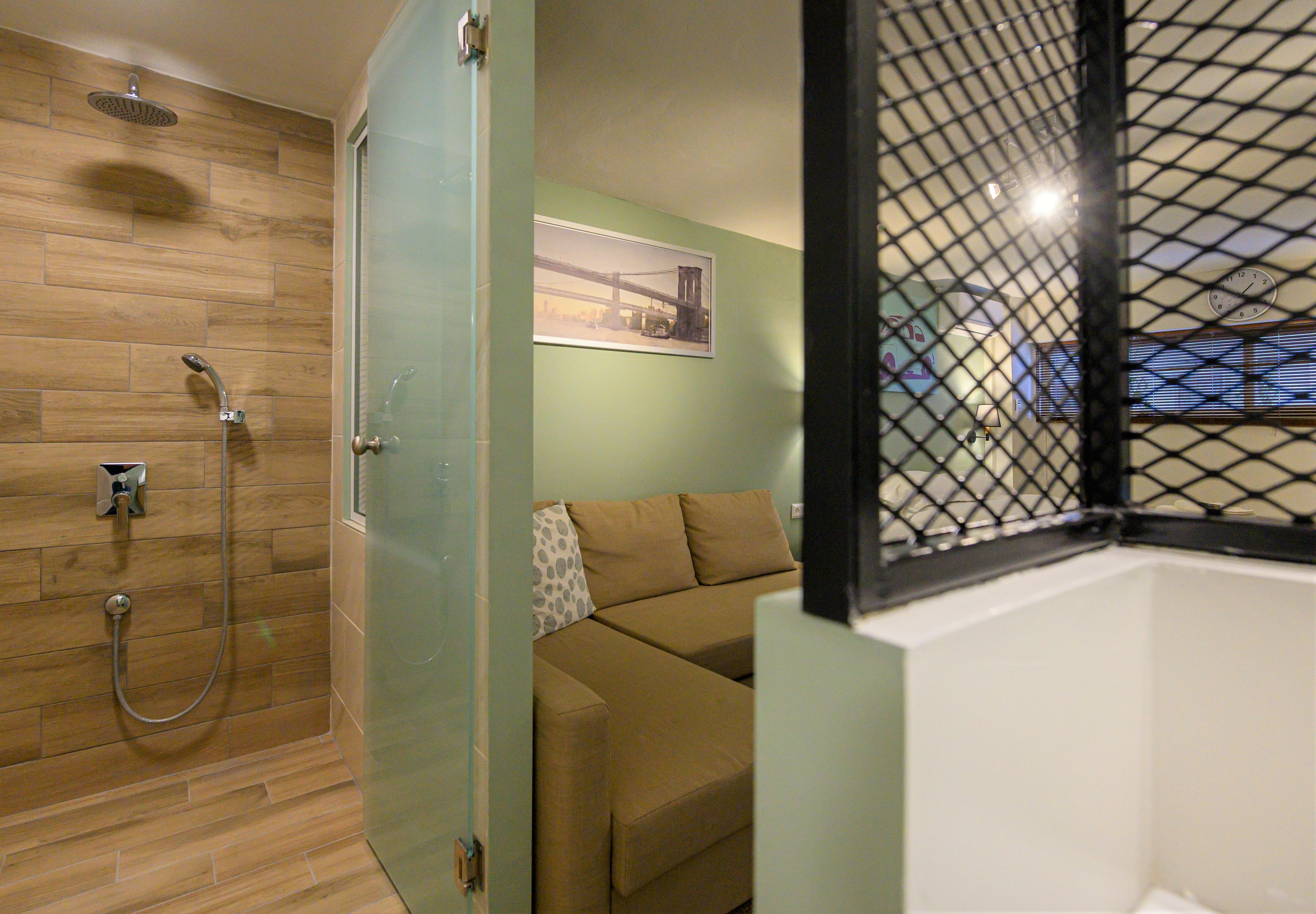 Ein Badezimmer mit Dusche, einer separaten Toilette mit Glaswand und einem beige gestreiften Sofa im angrenzenden Wohnbereich.