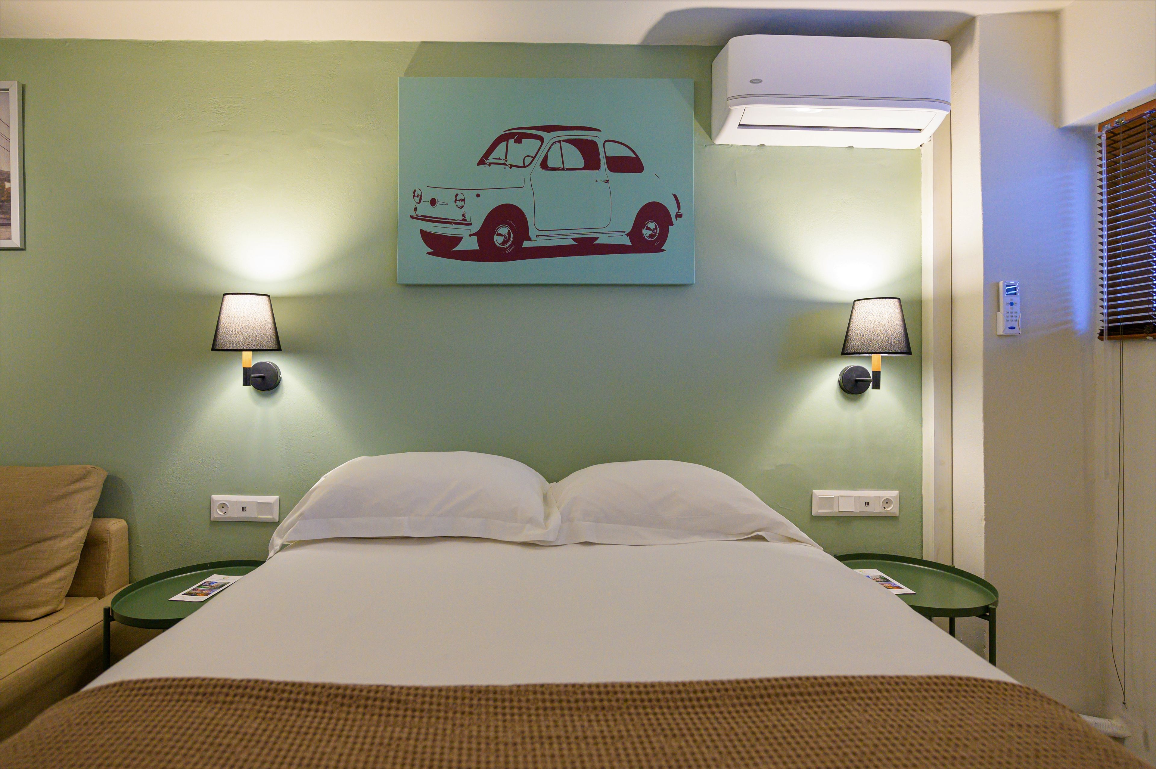 A hotel room with a bed, two nightstands, a wall-mounted lamp, and a wall painting of a car.