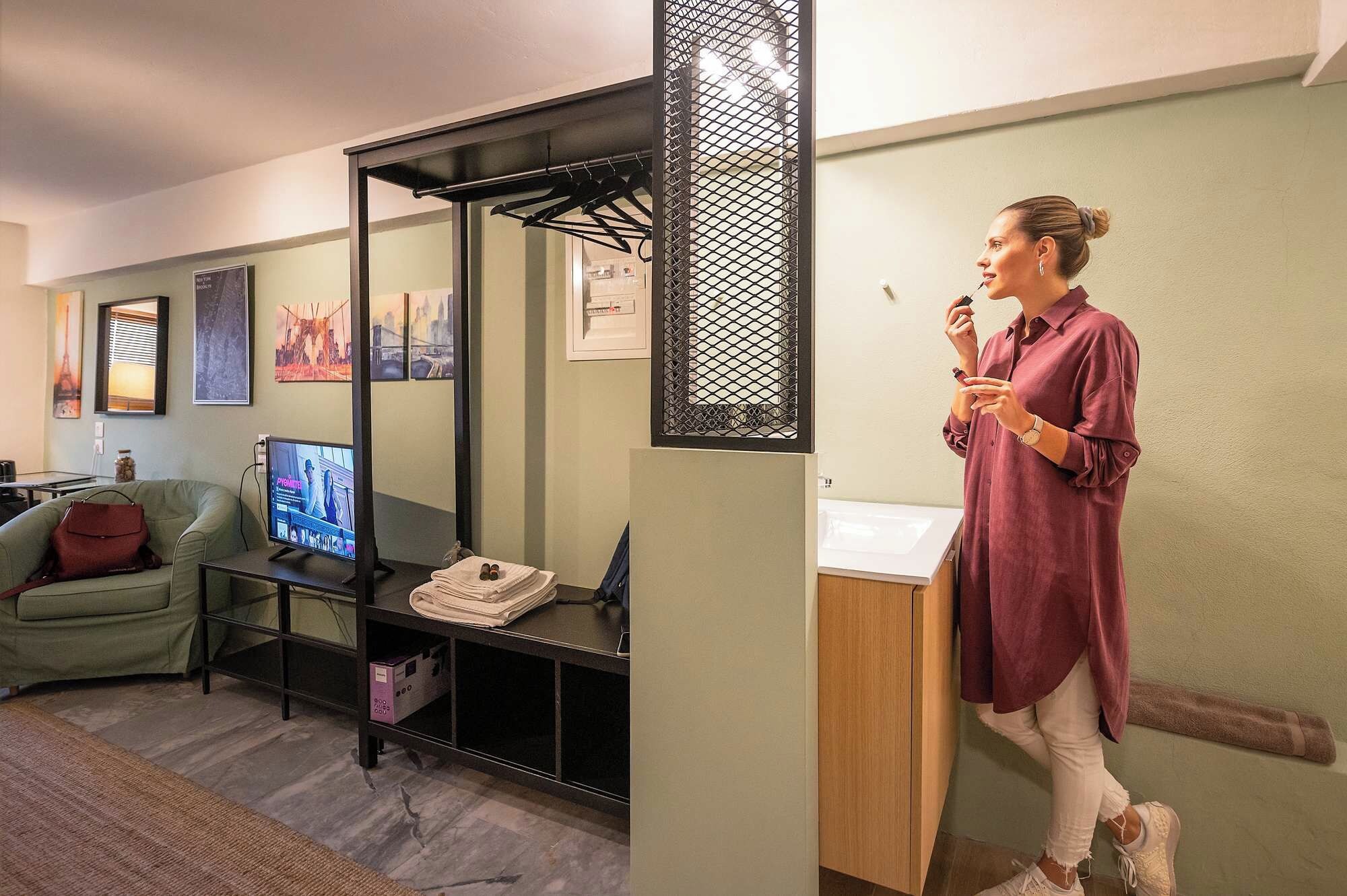 A person speaking into a microphone in a room with a television, a sofa, and a desk with a computer.