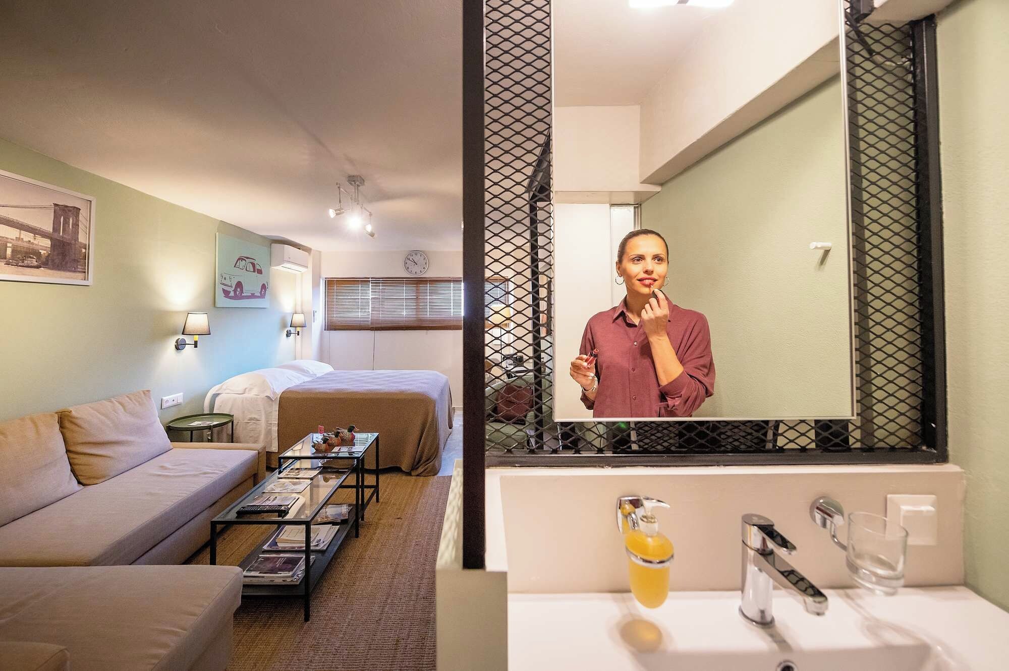 Habitación de hotel con cama, sofá, mesa de centro, espejo y baño con lavamanos y espejo.