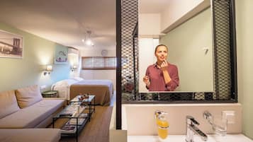 Habitación de hotel con cama, sofá, mesa de centro, espejo y baño con lavamanos y espejo.