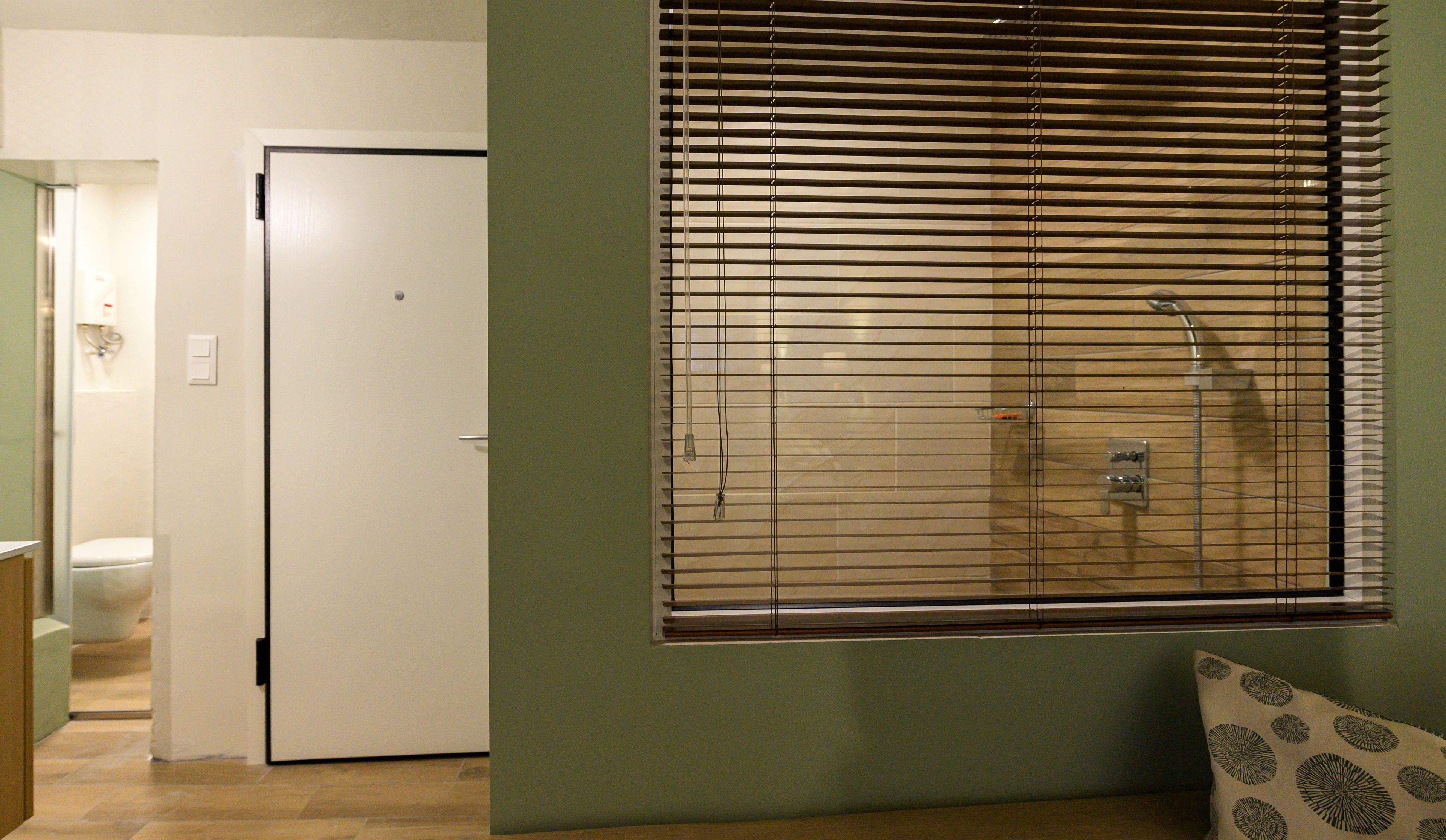 Ein Zimmer mit Dusche, Tür und Fenster mit Jalousien.