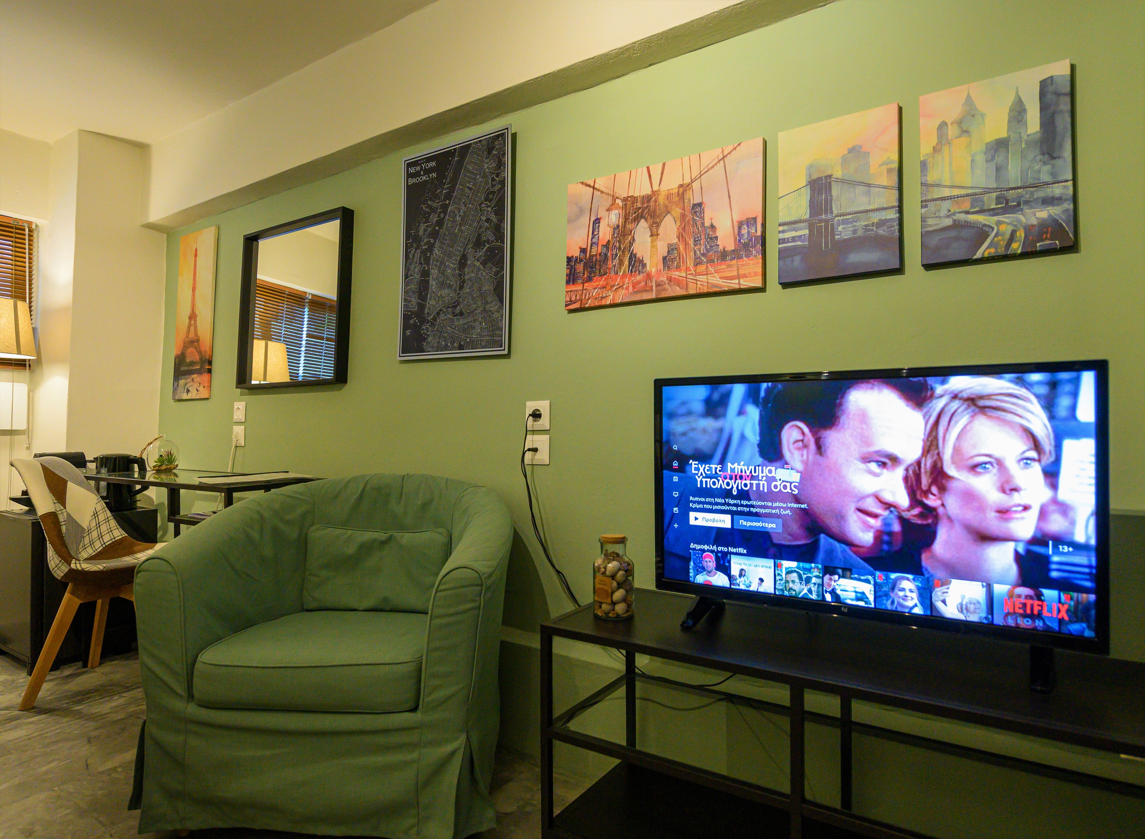 A living room with a green sofa, a TV on a stand, and wall art depicting cityscapes.