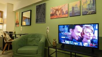 A living room with a green sofa, a TV on a stand, and wall art depicting cityscapes.