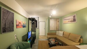 A living room with a sofa, a television, and artwork on the walls. - Pols Studio - Project Kalamata Mediterranean Suites (Kalamata)