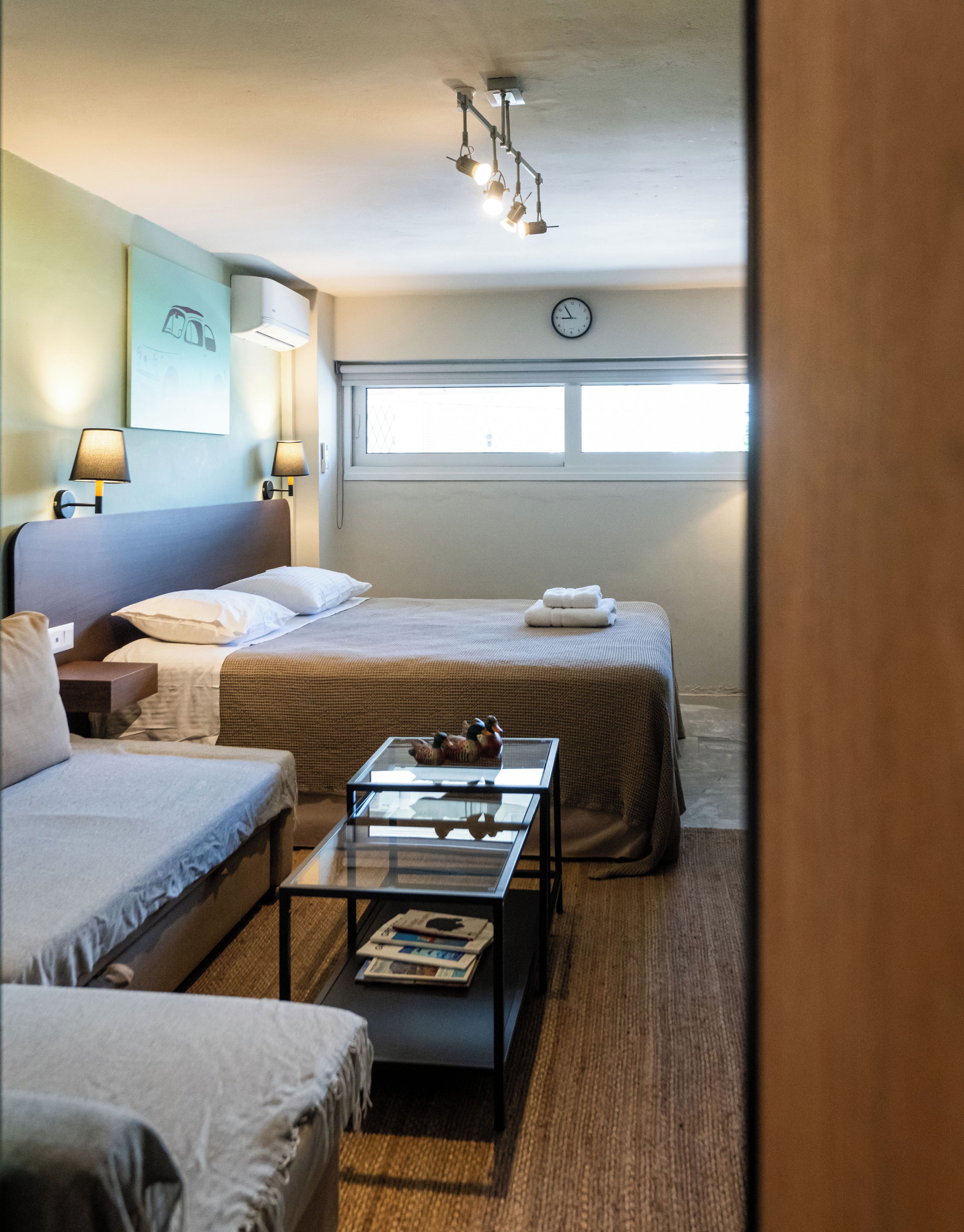 Een hotelkamer met twee bedden, een bank, een glazen salontafel en een wandklok.