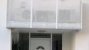 A building with a white facade, a balcony with potted plants, a door labeled 'HAATONUI 30', and a parked car.