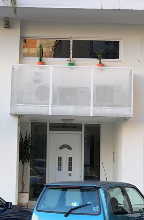 A building with a white facade, a balcony with potted plants, a door labeled 'HAATONUI 30', and a parked car.