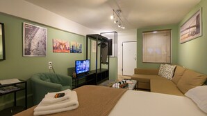 A hotel room with a bed, a green armchair, a television, and a sofa. - Pols Studio - Project Kalamata Mediterranean Suites (Kalamata)