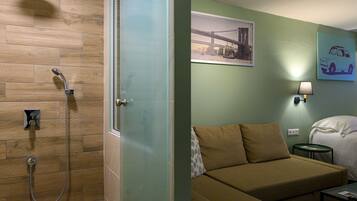 A hotel room with a shower, a bed, a sofa, a nightstand, and a wall-mounted lamp.
